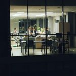 Colleagues collaborate in a glass-walled office at night, focused on tasks.