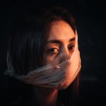A woman with her face covered in fabric portrays silence and introspection against a dark background.