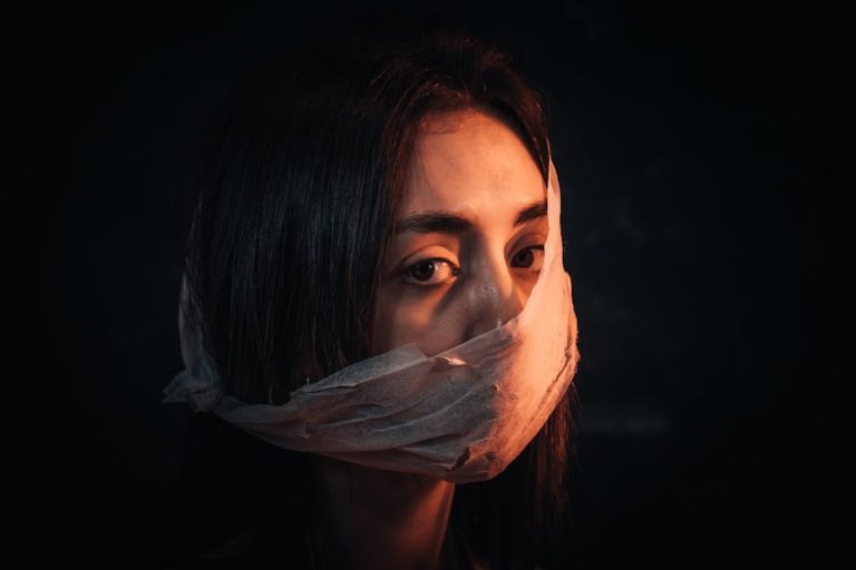 A woman with her face covered in fabric portrays silence and introspection against a dark background.