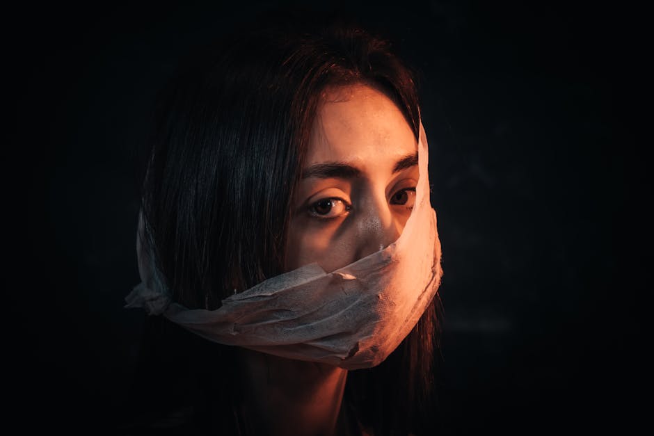 A woman with her face covered in fabric portrays silence and introspection against a dark background.