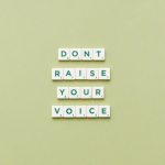 The Nocebo Effect: Why Your Leadership Narrative Can Make or Break Your Team Scrabble tiles spelling 'Don't Raise Your Voice' on a green background.
