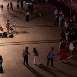 A lively night scene with a street performer and audience gathering on an outdoor promenade.