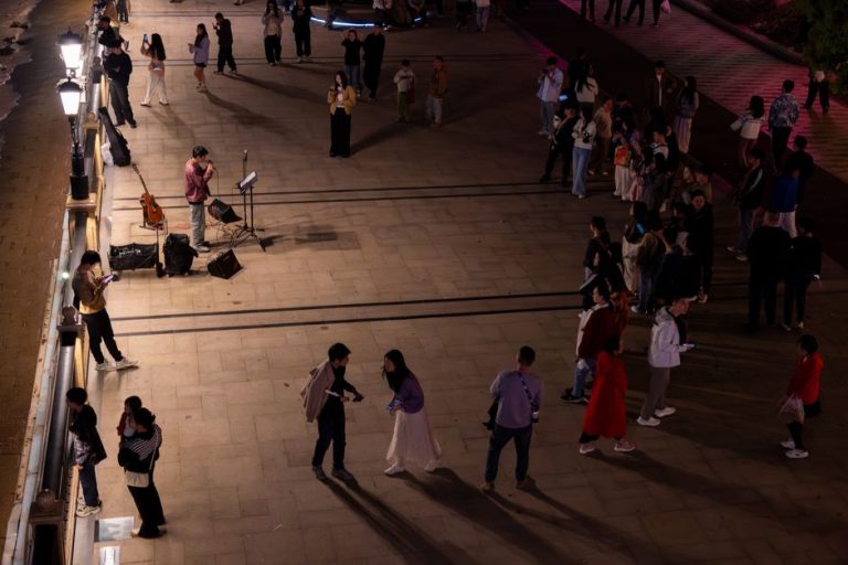 A lively night scene with a street performer and audience gathering on an outdoor promenade.