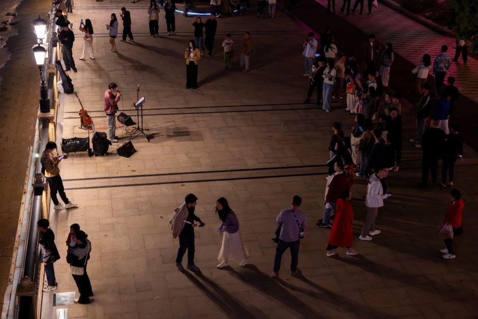 A lively night scene with a street performer and audience gathering on an outdoor promenade.