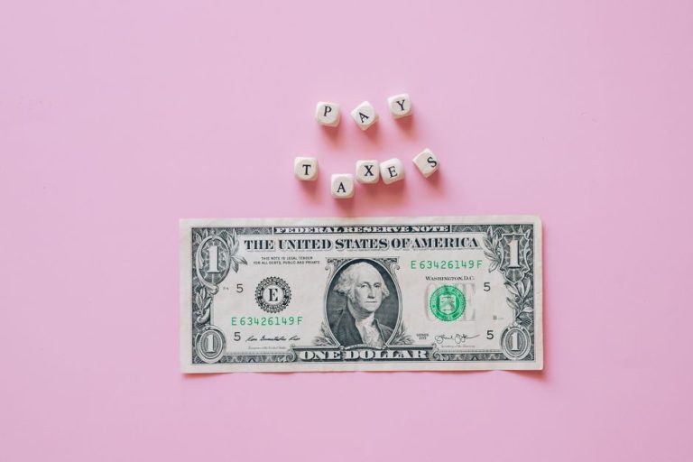 US one dollar bill on a pink background with pay taxes reminder cubes.