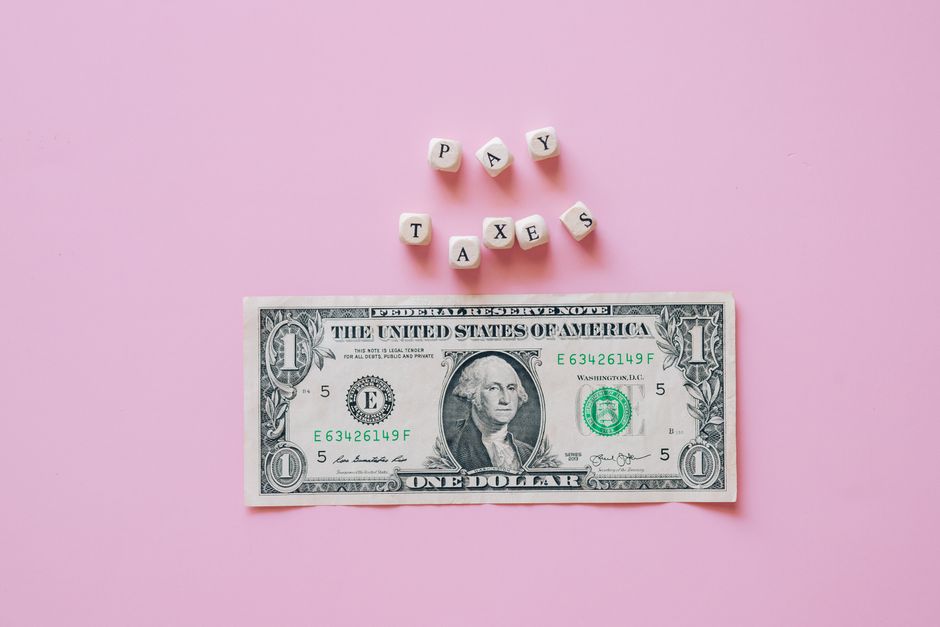 US one dollar bill on a pink background with pay taxes reminder cubes.