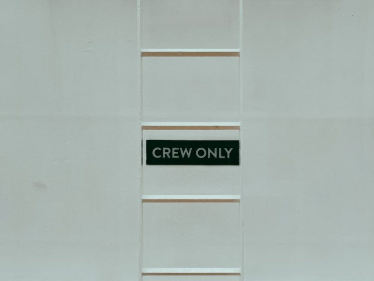 A minimalistic image featuring a 'Crew Only' sign on a ladder against a white wall.