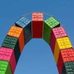 A vibrant display of stacked shipping containers forming an arch under a clear blue sky.