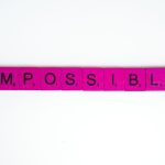 Pink scrabble tiles arranged to spell 'Impossible' on a white surface, close-up view.