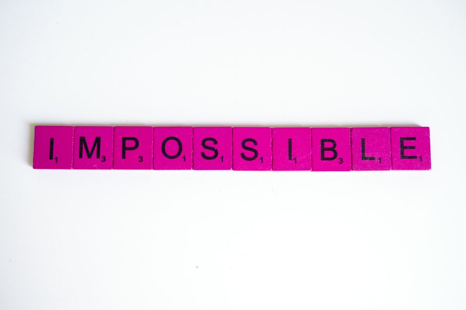 Pink scrabble tiles arranged to spell 'Impossible' on a white surface, close-up view.