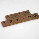 Scrabble tiles form an inspiring message 'Keep Trying' on a white background. Motivational and clean aesthetic.