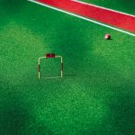 A vivid image of a gateball court showcasing a ball near the hoop on green artificial turf.