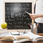 The Physics of Velocity: Lessons from Electromagnetic Launchers Woman writing physics equations on a blackboard with books and an apple on the desk.