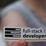 The Post-Growth Tech Stack: Why 'Minimalist Computing' is the Next Competitive Advantage A hand holding a sticker labeled 'full-stack developer', symbolizing technology and programming skills.