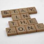 Wooden Scrabble tiles arranged to spell 'Stay in the Zone' on a white background.
