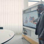Professional in suit presenting data on screen in a modern office environment.