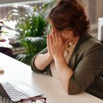 Businesswoman in wheelchair, tired at laptop, symbolizes office stress.