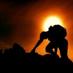 The Resilience Paradox: Why Peak Efficiency is Now Your Greatest Liability A silhouette of a man climbing rocks against a dramatic sunset sky, symbolizing adventure and determination.