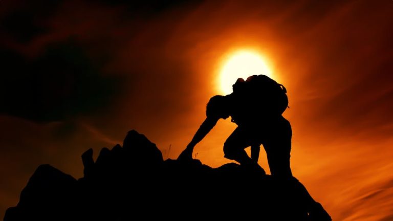 A silhouette of a man climbing rocks against a dramatic sunset sky, symbolizing adventure and determination.