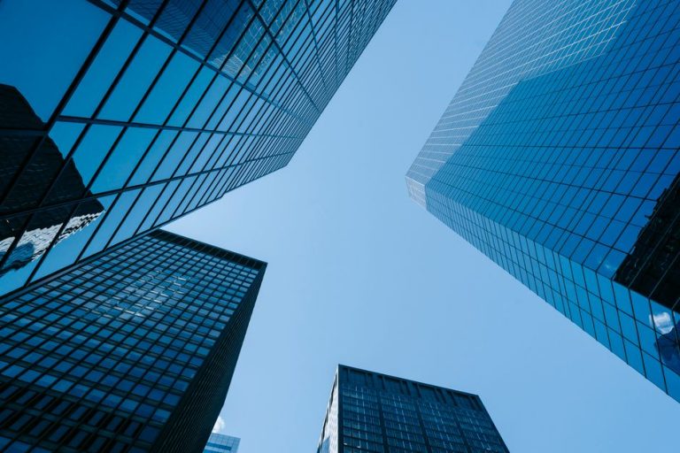 From below of contemporary high rise buildings with glass walls located on street with sunlight in modern district of city