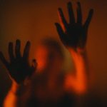 Mysterious silhouette of hands on frosted glass with dramatic red lighting.