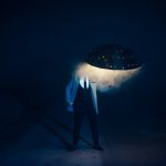A person in a suit stands in foggy darkness holding an LED-lit umbrella, creating a mysterious scene.