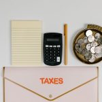 A flat lay of tax preparation essentials: calculator, coins, notepad, pen, and folder.