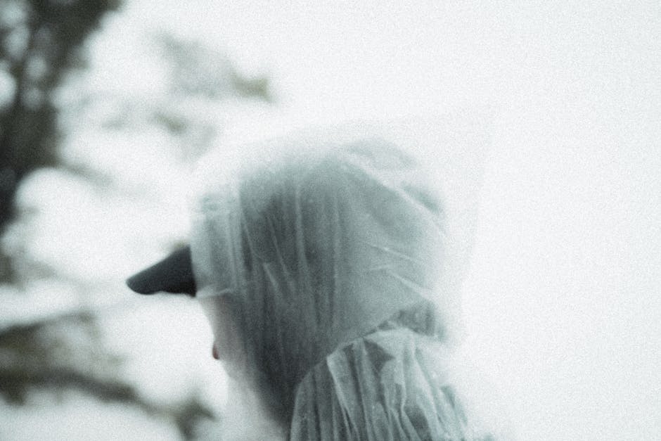 A moody close-up portrait of a man wearing a rain poncho, evoking a sense of solitude and introspection.