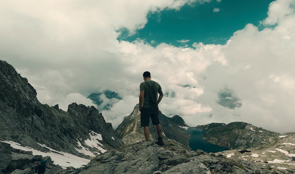 A lone hiker stands on a rocky mountain peak in Switzerland, gazing at a tranquil lake below.