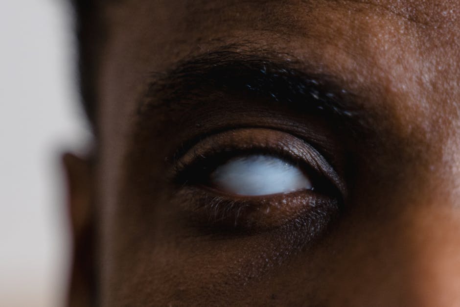 A detailed close-up photograph of an eye with a milky white appearance, representing blindness.
