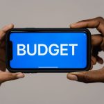 The Strategic Cost of Privacy: Competitive Advantage in Data Two hands hold a smartphone displaying the word 'budget' on a blue screen, symbolizing financial planning.