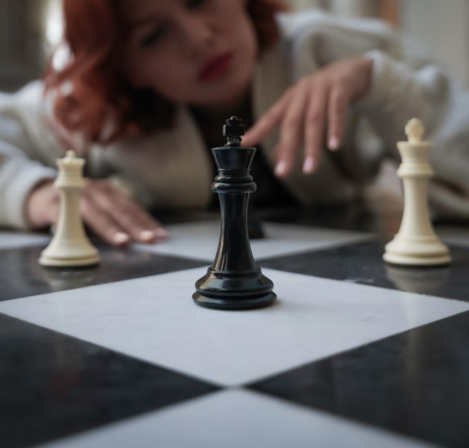 A woman focuses intently on chess pieces, illustrating strategy and concentration.