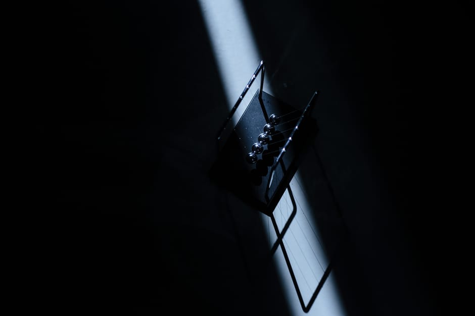 Newton's cradle in a dark room with striking light, showcasing physics concepts.