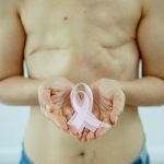 Crop unrecognizable topless woman with scars on breast after operation showing pink ribbon as sign of Breast Cancer day in light studio