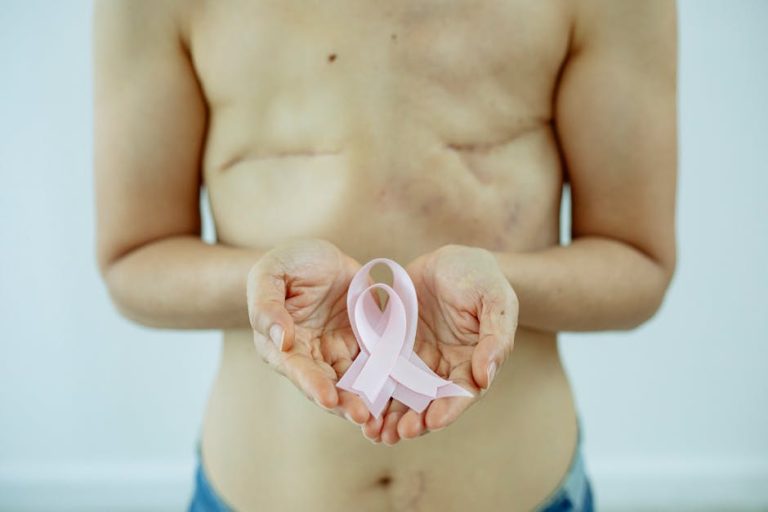 Crop unrecognizable topless woman with scars on breast after operation showing pink ribbon as sign of Breast Cancer day in light studio