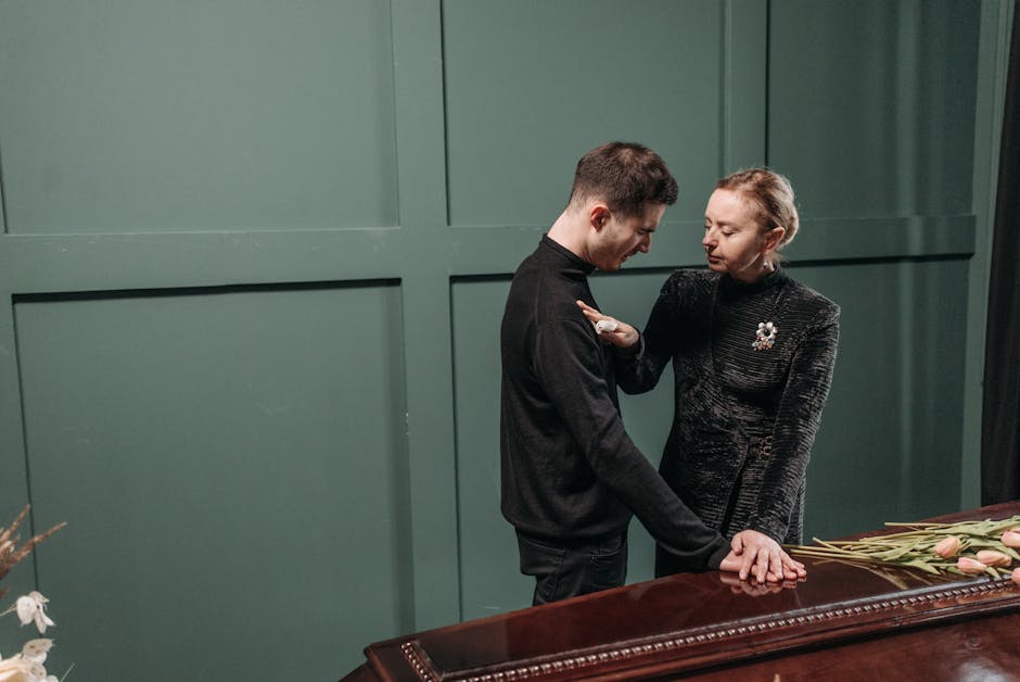A grieving man and woman comfort each other at a funeral, expressing sorrow and loss.