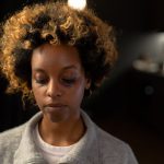 A woman with a bruise on her face, looking thoughtful in an indoor setting.