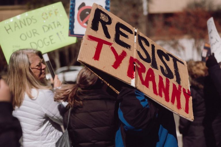 Protest scene with demonstrators holding signs expressing opposition to tyranny.
