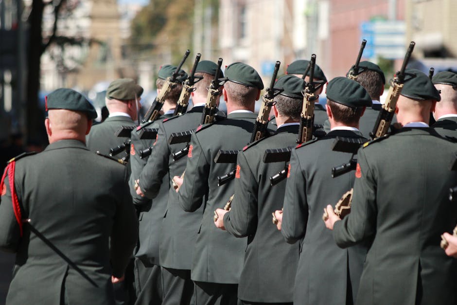 A group of soldiers in uniforms holding firearms, marching through a street in an outdoor formation.