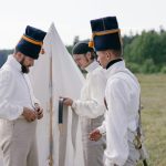 Men in historical military uniforms prepare for reenactment outdoors.