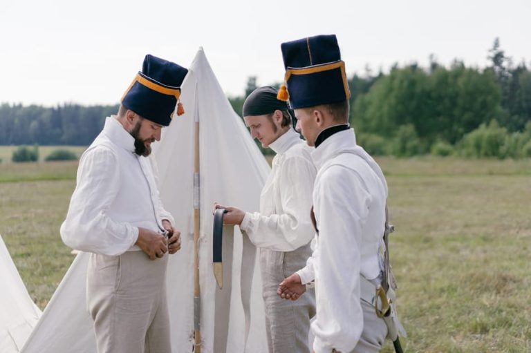 Men in historical military uniforms prepare for reenactment outdoors.