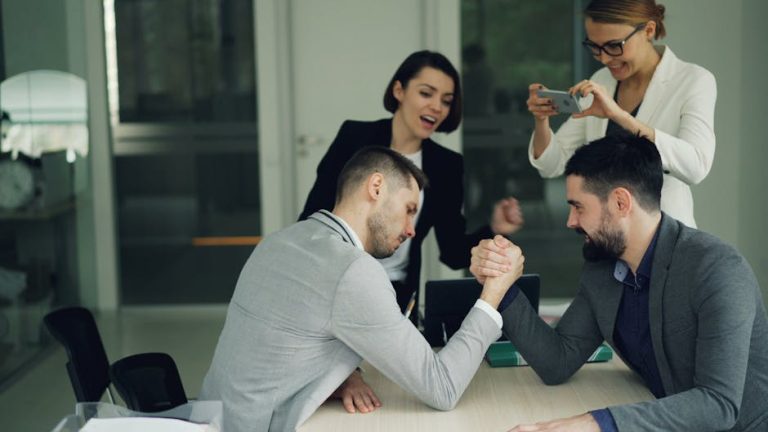 Colleagues cheer during a fun office arm wrestling challenge, fostering team spirit.
