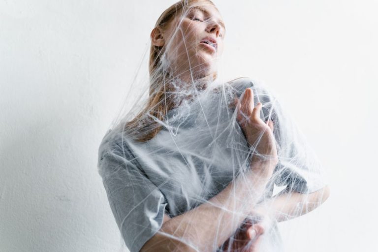 A woman enveloped in spider webs, representing anxiety and helplessness in an artistic conceptual shot.