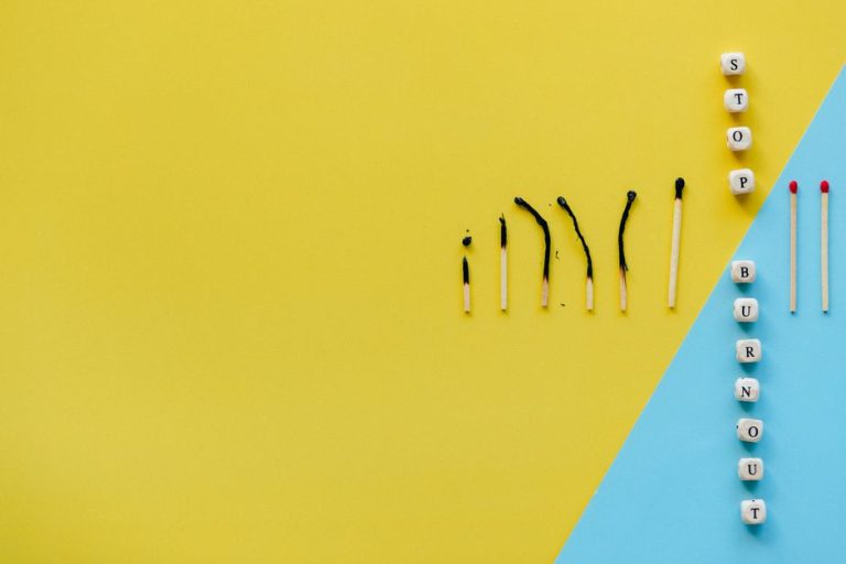Artistic representation of burnout using matches and blocks spelling 'STOP BURNOUT' on colorful background.