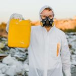 Toxic Waste Neutralization: A Strategic Framework for Leaders Worker in a protective suit holds a yellow container, monitoring pollution at a waste site.