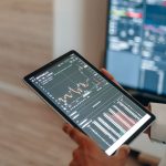 A person uses a tablet to monitor stock market trends and real-time trading graphs.