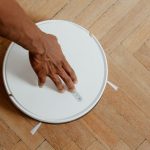 Vacuum 14 and Operational Excellence: Engineering Silence A close-up of a hand activating a robotic vacuum cleaner on a wooden floor.
