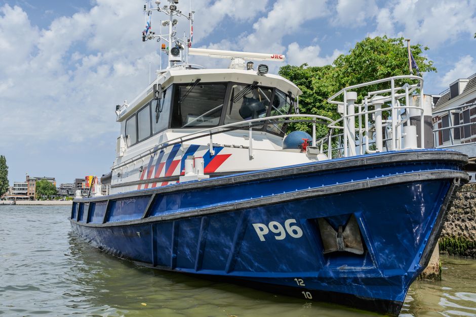 A close-up view of a P96 patrol boat moored by a riverbank under a clear sky.