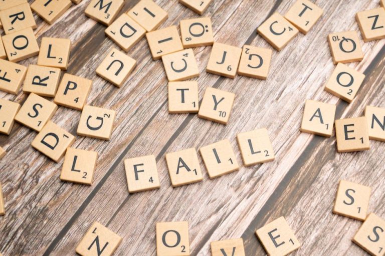Scrabble tiles on wood form 'FAIL', symbolizing defeat and reflection.