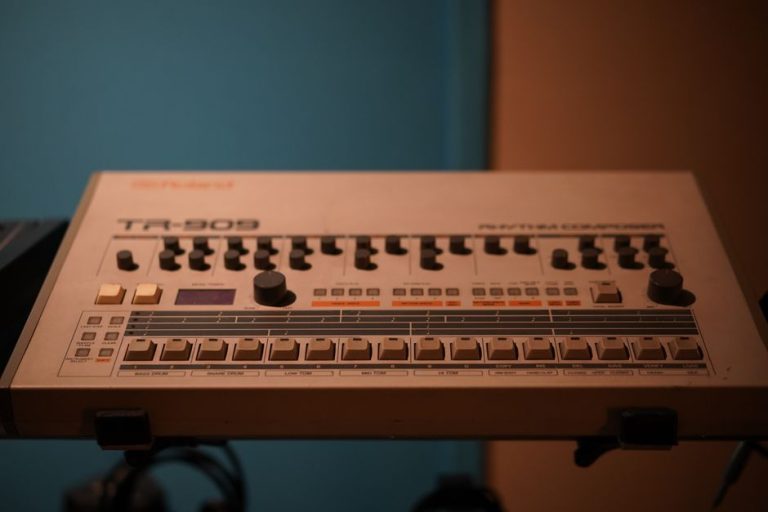 Close-up of a classic Roland TR-909 drum machine in a studio setting.